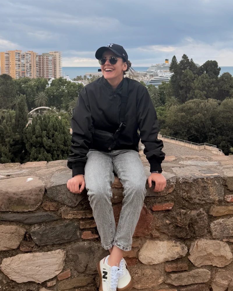 Milica, Saldo's founder, sitting on a stone wall above the city and the sea